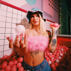 Model wearing 2000's era inspired fashion while modeling baby pink acrylic press-on nails with fine iridescent holographic glitter while standing in a pink plastic ball pit.